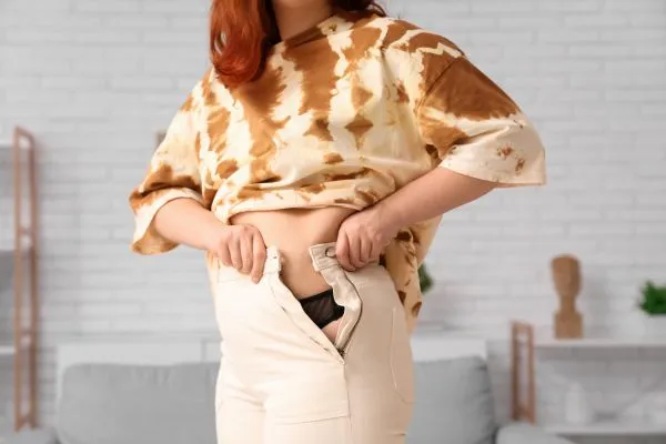 Image of woman trying to do her trousers up after pregnancy weight gain West Drayton